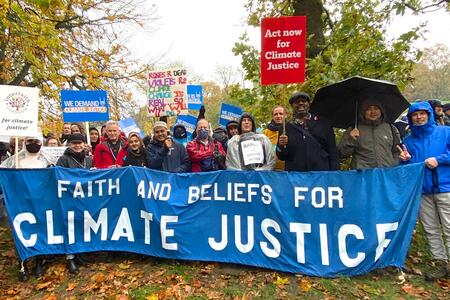 Pictures of various faith leaders standing in the rain holding a banner that says Faith and Beliefs for Climate Justice
