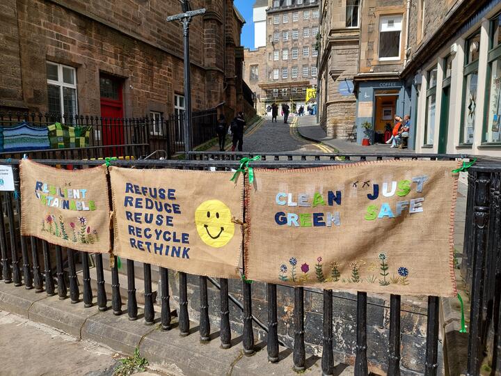 Three banners tied to a railing on an Edinburgh Street. They are hessian with words appliqued on. Left it says "Resilient, Sustainable", middle "Refuse, Reduce, Reuse, Recycle, Rethink", right "Clean, Just, Green, Safe"