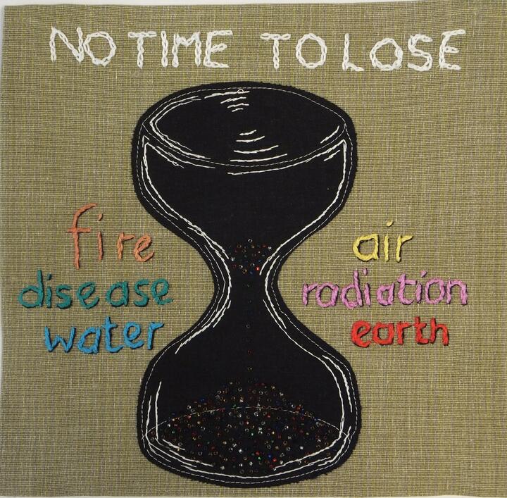 Appliqued panel, created by Quakers working with the Loving Earth Project. An appliqued panel with a sandtimer in the centre, beads trickling through the sandtimer. In embroidered letters above the time it says "No Time To Lose". To the left of the time it says "fire, disease, water". To the right "air, radiation, earth",