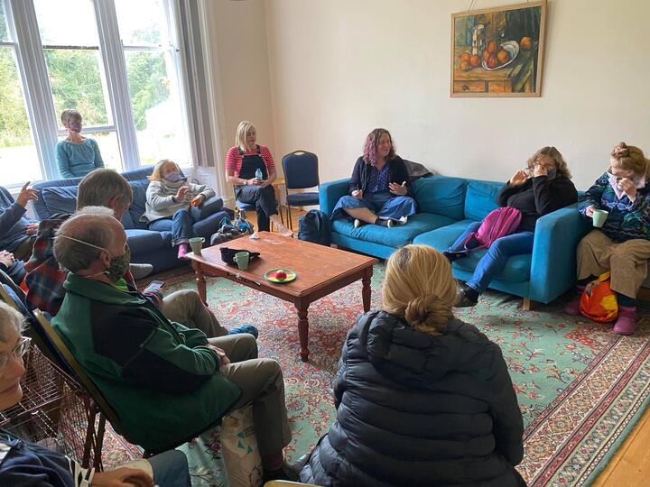 Zoe sitting cross-legged in a cozy room, in discussion with other Quakers