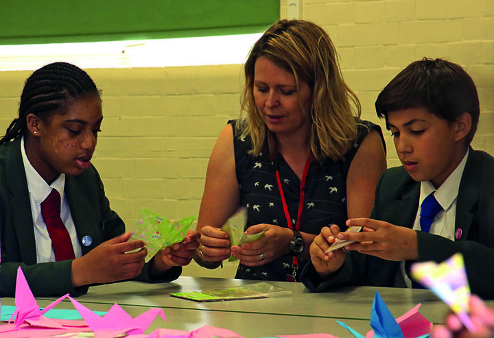 Two children and an adult woman make peace cranes.